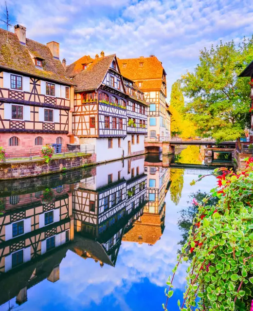 Maisons à colombages colorées dans le quartier historique de la Petite France à Strasbourg, se reflétant parfaitement dans les eaux calmes de l'Ill par une journée ensoleillée.