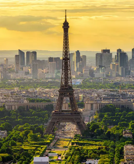 Vue panoramique emblématique de la Tour Eiffel à l'heure dorée, surplombant le Champ de Mars verdoyant vers les gratte-ciel modernes de La Défense.