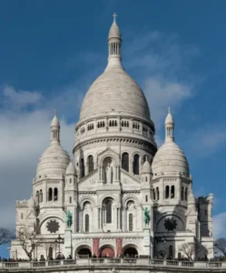 Vue de face des dômes blancs de la basilique du Sacré-Cœur sur un ciel bleu clair.