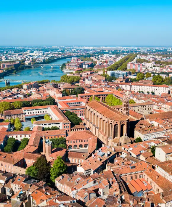 Vue panoramique aérienne de la « Ville Rose », un secteur stratégique pour une agence SEO Toulouse, dévoilant les denses toits de tuiles rouges, la Garonne et l'imposante basilique Saint-Sernin.