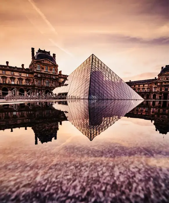 Prise de vue verticale de la pyramide et du palais du Louvre au coucher du soleil, se reflétant dans l'eau de la cour.