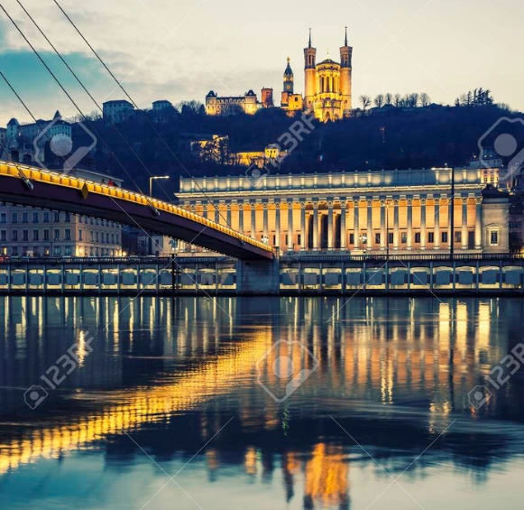 La façade néo-classique du Palais de Justice de Lyon avec ses 24 colonnes, vue de l'autre côté de la Saône au crépuscule avec le pont de la Feuillée.
