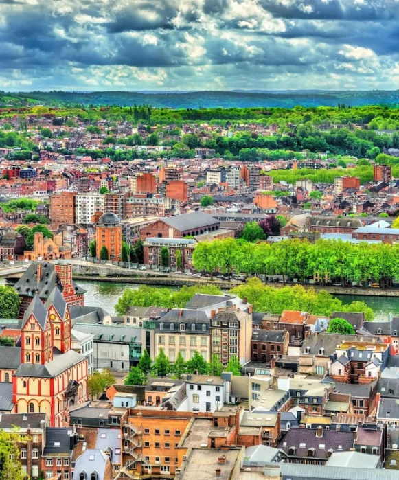Vue en hauteur sur le centre historique de Liège, mettant en évidence les tours jumelles rouges et blanches de la collégiale Saint-Barthélemy au cœur du paysage urbain.