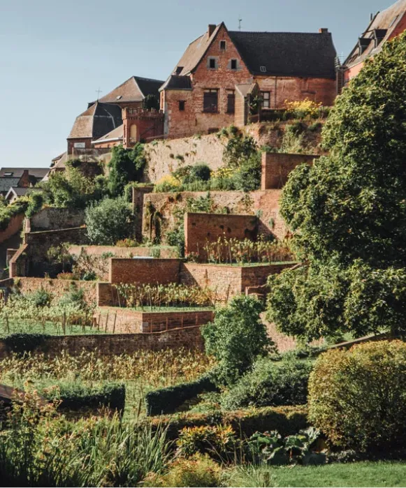 Vue ensoleillée des jardins suspendus de Thuin, montrant les murs de briques en terrasses et la végétation grimpant vers la ville haute.