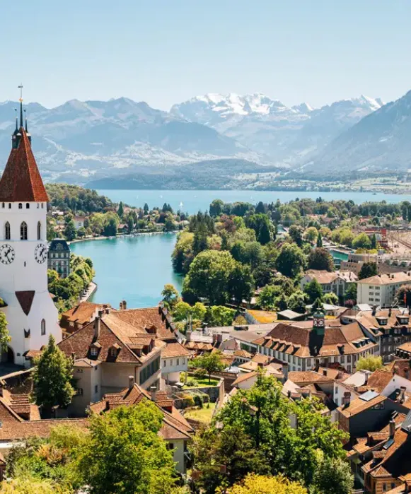 Vue en hauteur des toits rouges de Thoune, s'ouvrant sur le lac turquoise et les Alpes enneigées au loin.