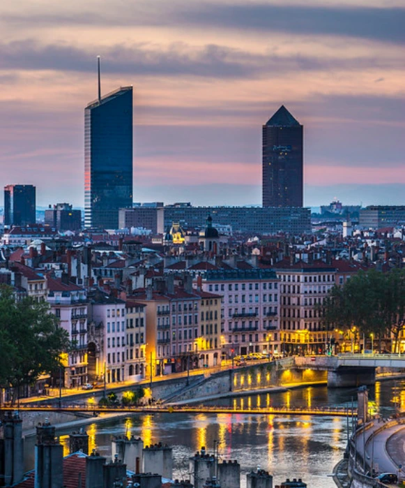 La Part-Dieu à Lyon au crépuscule, avec les tours « Crayon » et « Incity » illuminées sur un ciel rose et violet, surplombant la Saône.