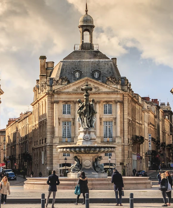 Passants autour de la fontaine des Trois Grâces sur l'emblématique place de la Bourse, chef-d'œuvre de l'architecture classique française.