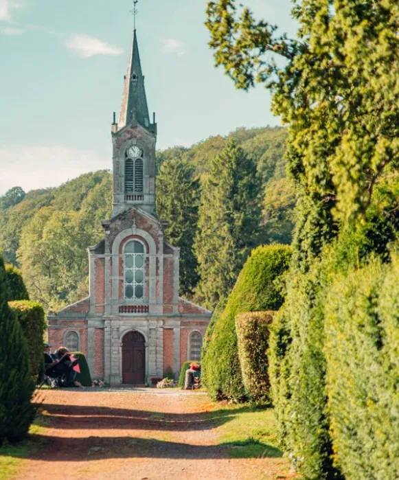 ue en perspective d'une charmante église en briques nichée dans la vallée verdoyante de l'Abbaye d'Aulne, entourée de grands arbres et de haies taillées.
