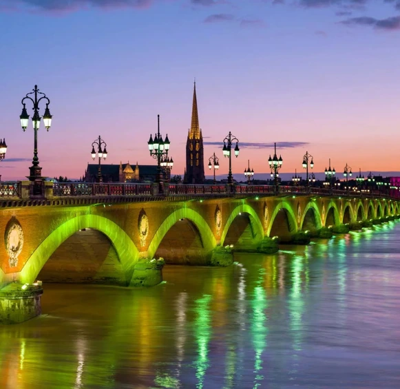 Le pont de Pierre historique au coucher du soleil, ses arches en pierre et ses lampadaires ornementés se reflétant dans la Garonne.