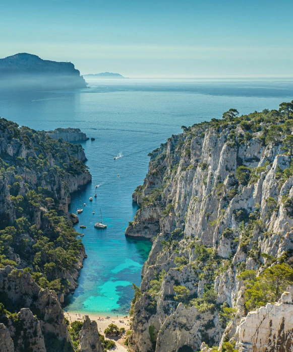 Vue en plongée de la calanque d'En-Vau, montrant les falaises de calcaire abruptes et les eaux turquoise parsemées de quelques bateaux.