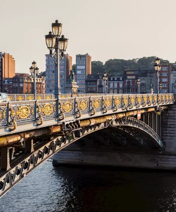 Gros plan sur l'ornementation du pont de Fragnée, montrant ses garde-corps décorés de détails dorés et ses lampadaires classiques enjambant le fleuve.
