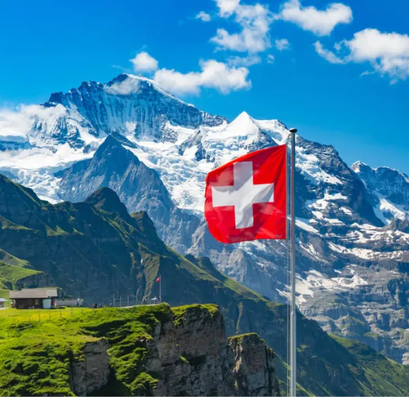 un drapeau suisse flottant au vent avec en arrière-plan le sommet enneigé de la Jungfrau sous un ciel bleu éclatant.