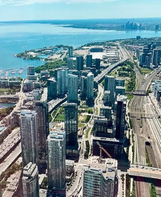 Une vue aérienne en plongée du centre-ville de Toronto, montrant la forte concentration de gratte-ciel modernes en verre bordant les rives du lac Ontario.