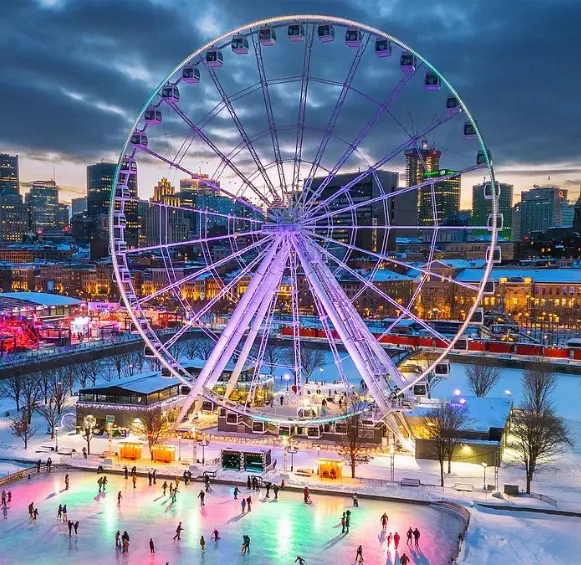 Une soirée magique au Vieux-Port de Montréal, montrant la Grande Roue et une patinoire extérieure illuminée par des lumières colorées sur fond de paysage urbain hivernal.