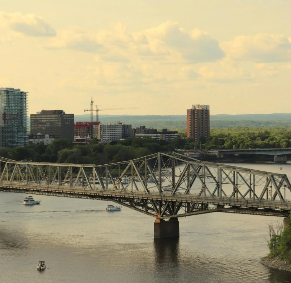 Vue d'ensemble du pont Alexandra historique enjambant la rivière des Outaouais, avec la silhouette urbaine de Gatineau et des immeubles modernes en arrière-plan.