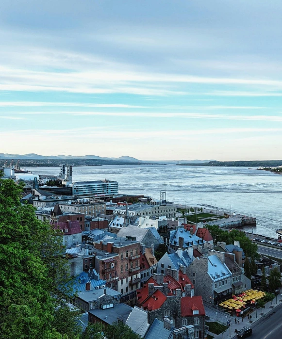 ue aérienne verticale surplombant les toits colorés du quartier Petit Champlain et les vastes eaux du fleuve Saint-Laurent sous un ciel doux.