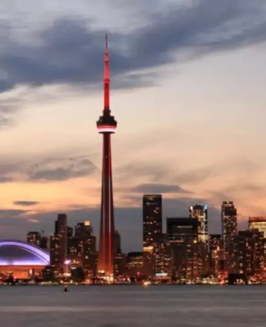La silhouette illuminée de Toronto au crépuscule, dominée par la tour CN éclairée en rouge se reflétant dans les eaux calmes du port.