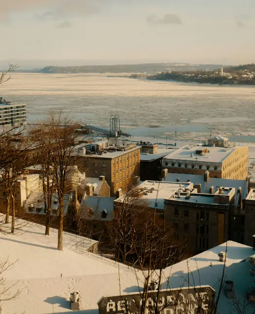 Une vue en hauteur des toits du Vieux-Québec surplombant le fleuve Saint-Laurent rempli de glaces à la dérive pendant l'hiver.