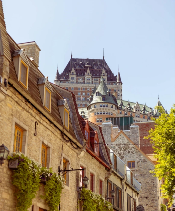 Vue depuis une ruelle historique du Vieux-Québec montrant des bâtiments en pierre fleuris, avec les tours emblématiques du Château Frontenac s'élevant à l'arrière-plan.
