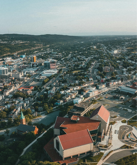 Une vue aérienne en plongée de la ville côtière de St. John's, montrant l'étendue urbaine, le port et les collines à l'horizon.