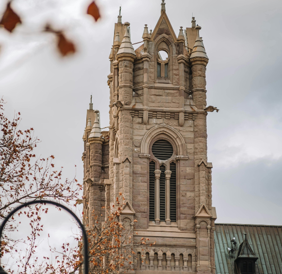 Vue détaillée de la tour d'horloge en pierre d'un bâtiment historique de style gothique à Kingston, en Ontario, encadrée par des feuilles d'automne.