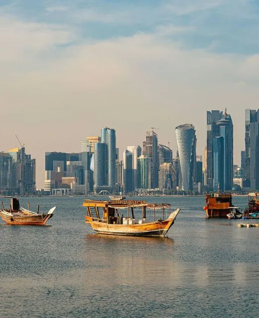 Embarcations traditionnelles en bois naviguant devant la skyline de Doha.
